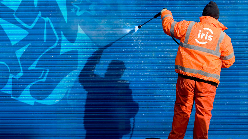 Une personne efface des graffitis sur un mur bleu.