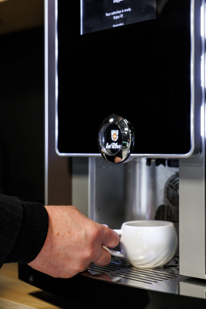 Hand places cup under coffee machine tap.