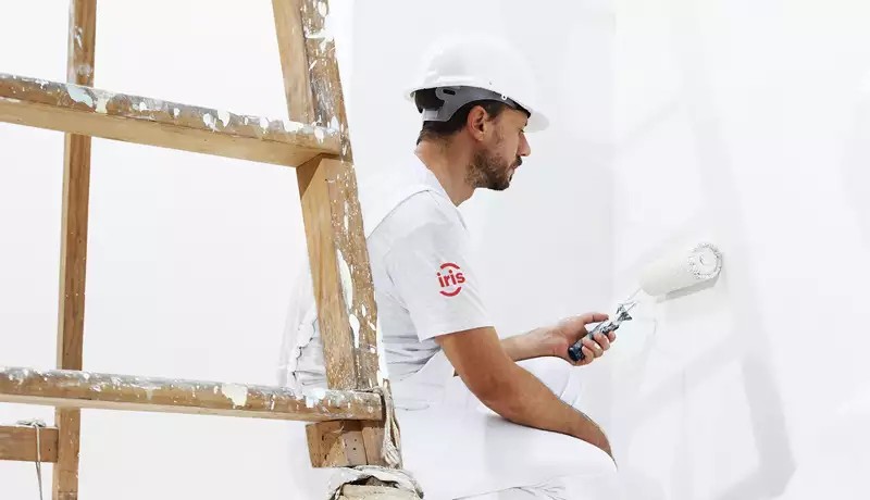 Le peintre peint un mur blanc au rouleau.